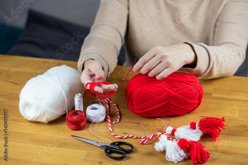 Woman making handmade traditional martisor, from red and white strings with tassel. Symbol of holiday 1 March, Martenitsa, Baba Marta, beginning of spring in Romania, Bulgaria, Moldova photo