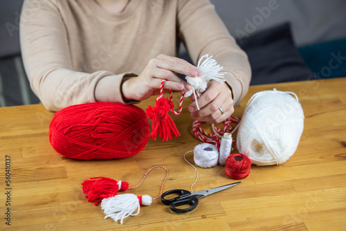 Woman making handmade traditional martisor, from red and white strings with tassel. Symbol of holiday 1 March, Martenitsa, Baba Marta, beginning of spring in Romania, Bulgaria, Moldova photo