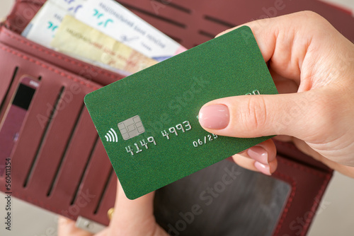 Woman's hands holding a green credit card and burgundy wallet with Ukrainian Hryvnias, close up. Banking, cashless payments, financed, purchases and money concept