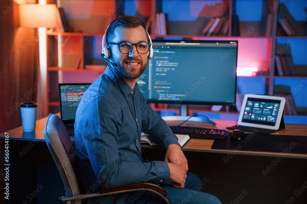 Positive professional programmer is working indoors and smiling. Neon lighting
