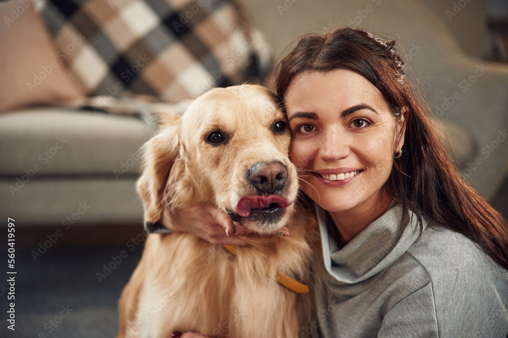Looking at the camera. Woman is with golden retriever dog at home