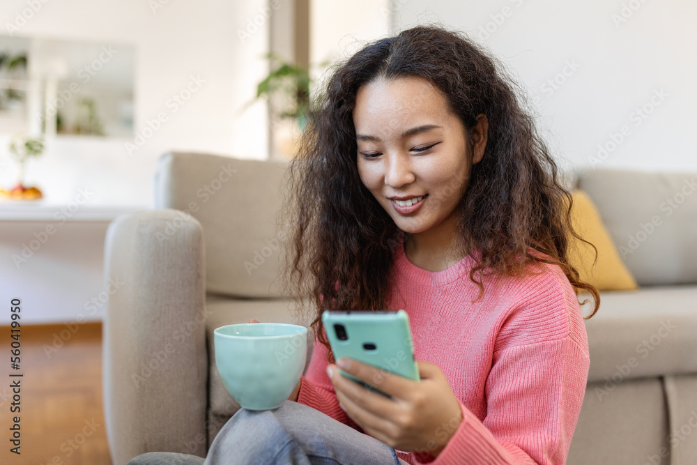 Attractive smiling Asian woman using smart phone while sitting on the sofa at home. Communication and video call concept. Attractive smiling Asian woman using smart phone while sitting on the sofa at home. Communication and video call concept.