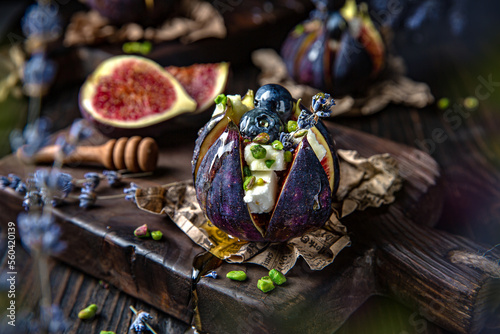 Figs baked with goat cheese, pistachios and honey, decorated with berries and lavender. Vegetarian delicacy. Beautiful still life for a poster. Shot in low key. Image for restaurant interior.