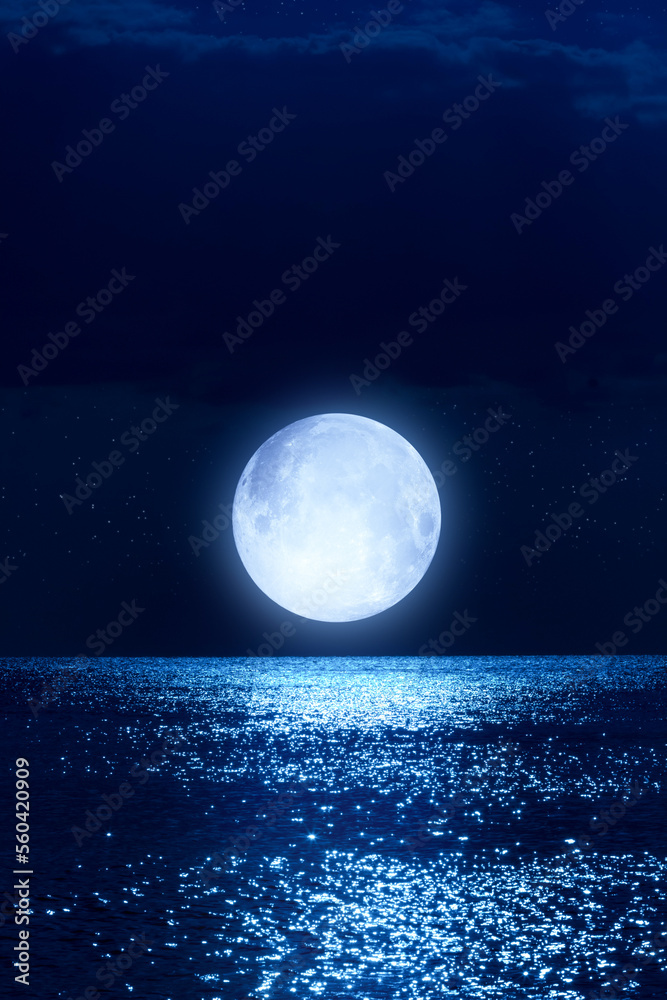 Full Moon with starry skies rising above ocean horizon.