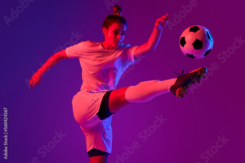 Leg kick. Young professional female football, soccer player in motion, training, playing over gradient pink background in neon light