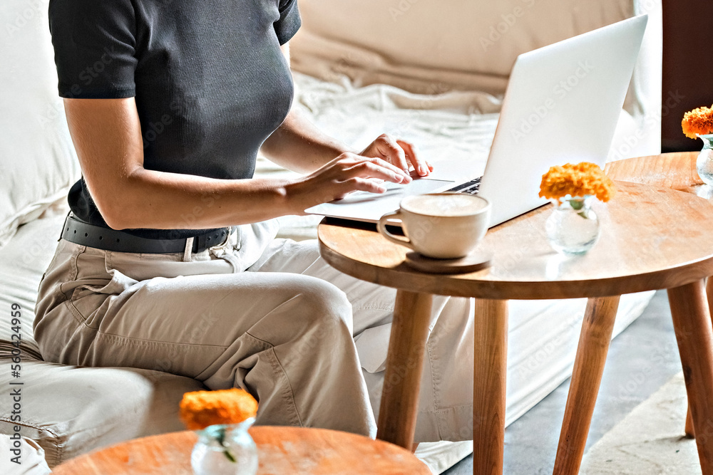 Fototapeta premium Woman with a cup of coffee working at laptop face unrecognized
