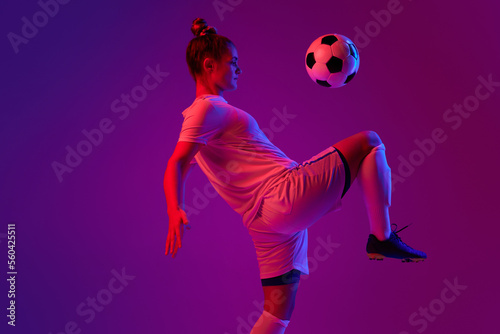 Knee kick. Young professional female football, soccer player in motion, training, playing over gradient pink background in neon light