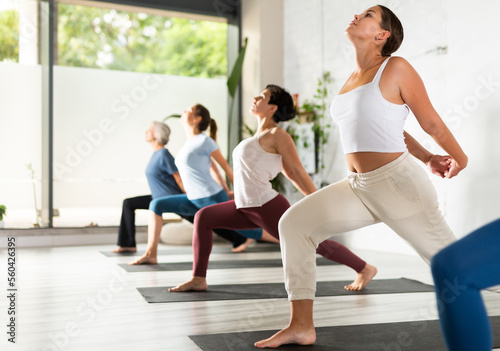 Active woman with group of adult people doing stretching workout for body flexibility in yoga studio