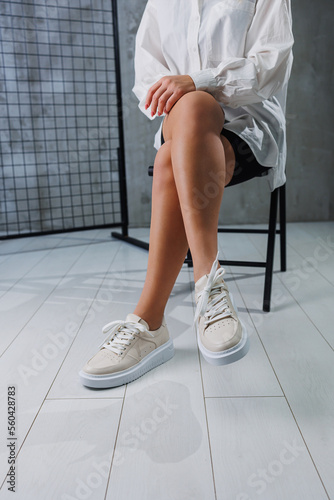 Female slender legs in beige casual sneakers with laces. Women's stylish leather summer shoes