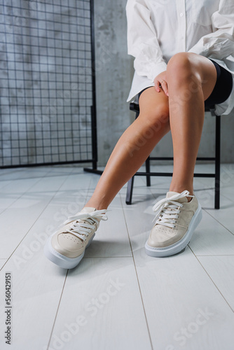 Female beautiful legs in beige casual sneakers. Women's stylish leather summer shoes