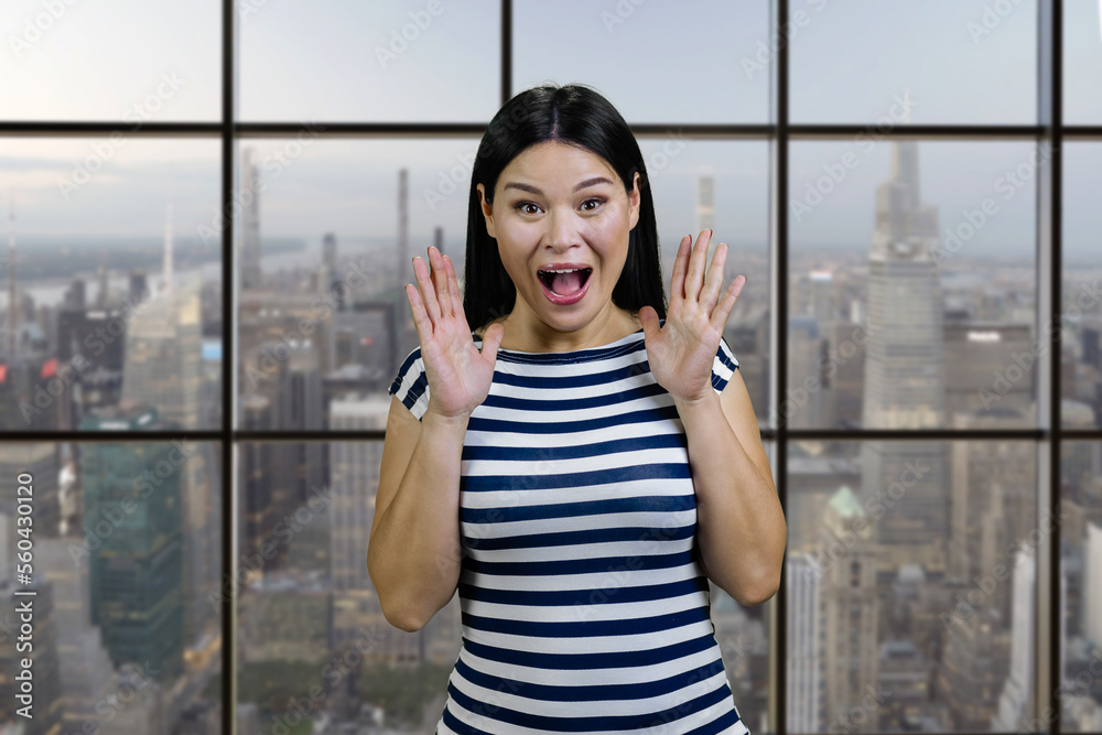 Portrait of a screaming yelling asian woman indoors. Checkered windows background with cityscape view.