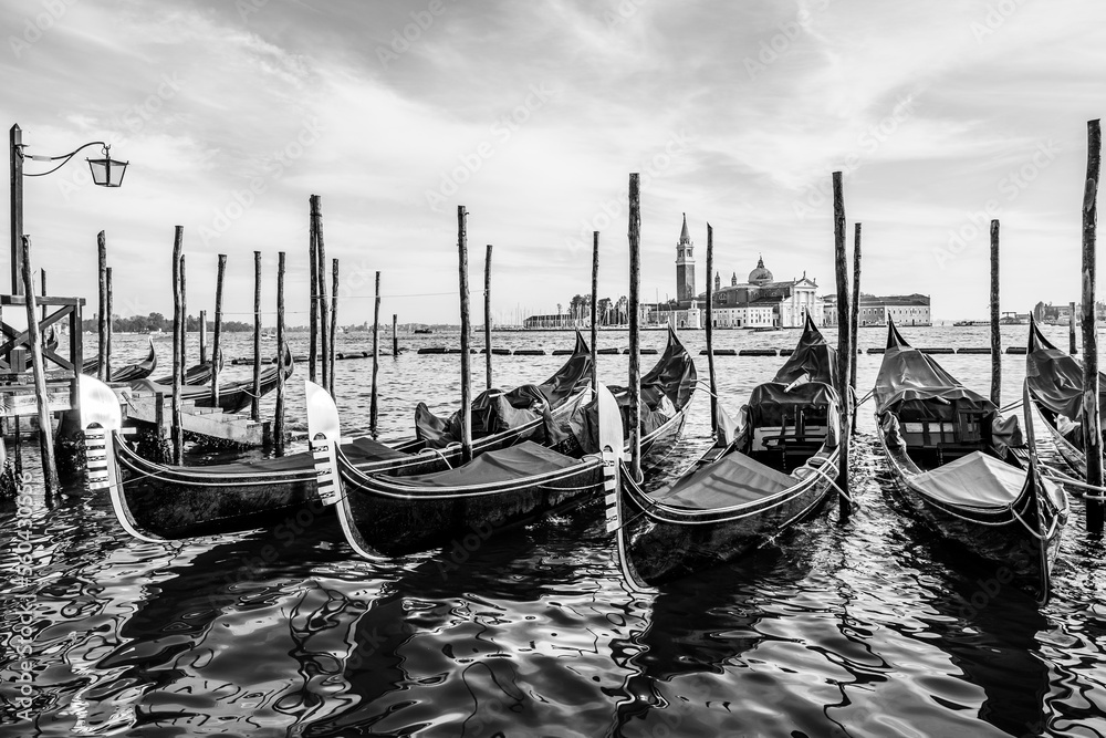 Gondolas floating by the shoreline of San Marco Square in front of the Island of San Giorgio Maggiore in Venice, Italy in black and whiye