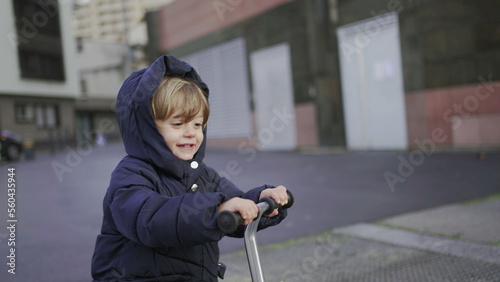 Happy toddler boy riding scooter outside on sidewalk, active child rides scooter2 photo