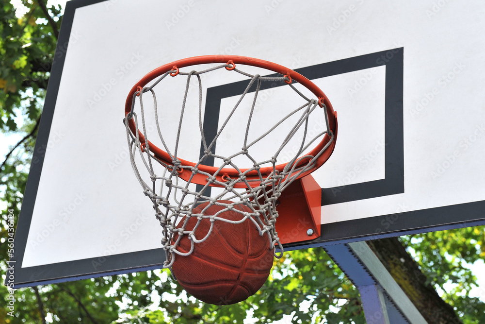 A basketball in a basket on an outdoor basketball court.