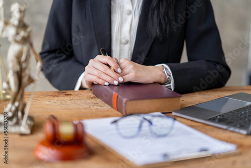 Professional Asian female lawyer or legal advisor sitting at her desk holding hands on books on justice concept Sections in the law that govern the conduct.