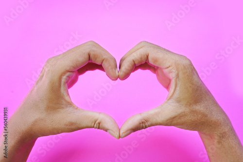 asian man hand forming a heart shape using the index finger and thumb  love symbol on pink background.  