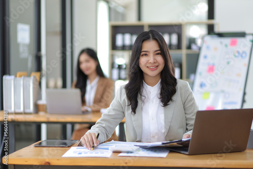 Attractive young Asian businesswoman working at her desk and having coworkers in the office.