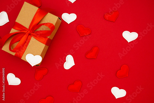 Gift box with red bow on red background with hearts around. Holiday banner. Top view