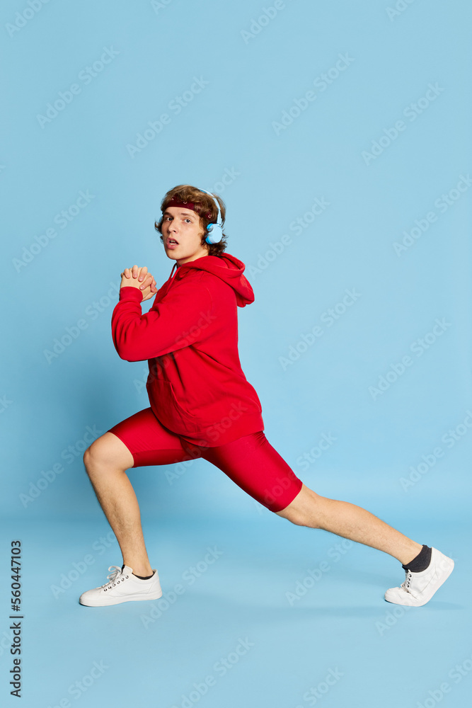 Workout. Young happy cheerful man in red sportswear isolated over blue background. Concept of active healthy lifestyle, positive emotions, sport, fitness, ad