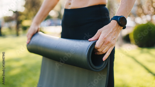 Close-up of hands of unrecognizable young woman rolling yoga mat after exercising at city park. Healthy lifestyle, sport.