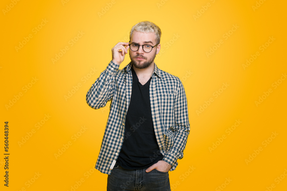 Young caucasian man looking suspicious through eyeglasses, uncertain, examining you, isolated over yellow background.