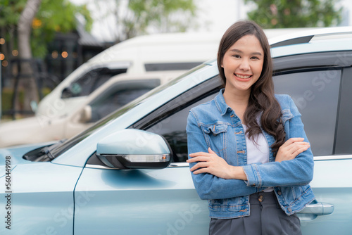 Asia woman leaning against the EV car at charging station and arm crossed with smile. Car driven by electric motor engine for clean environment. Rechargeable vehicle concept. Ecology green technology