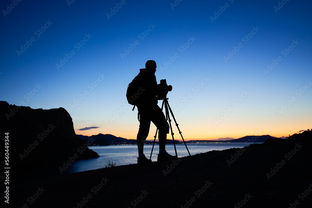 Silhouette of photographer on top of mountain at sunset background. Nature photographer in the action. Film analog photography