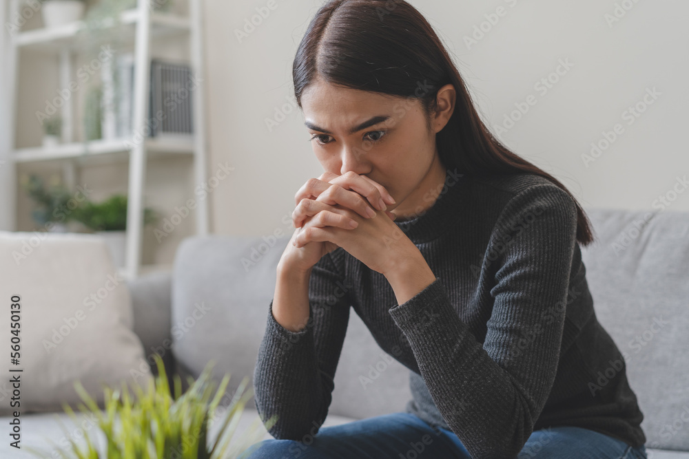 Unhappy anxiety young Asian woman sitting on the sofa at home. Unhappy anxiety young Asian woman sitting on the sofa at home.