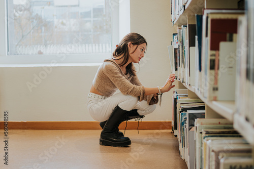 Focused Asian female student choosing book in library photo