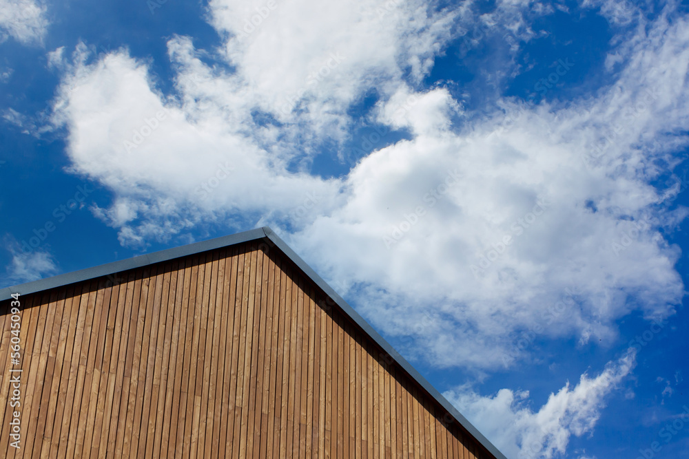 Wooden plank gabled roof on a new modern house against a blue sky with picturesque clouds. Wooden plank gabled roof on a new modern house against a blue sky with picturesque clouds.