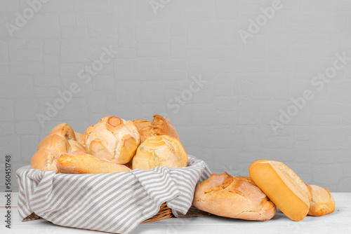 Fresh italian wheat breads in the basket on the table on white wall background. Homemade baked various loaves of wheat, assorted grain breads and bun. Bread background, copy space photo