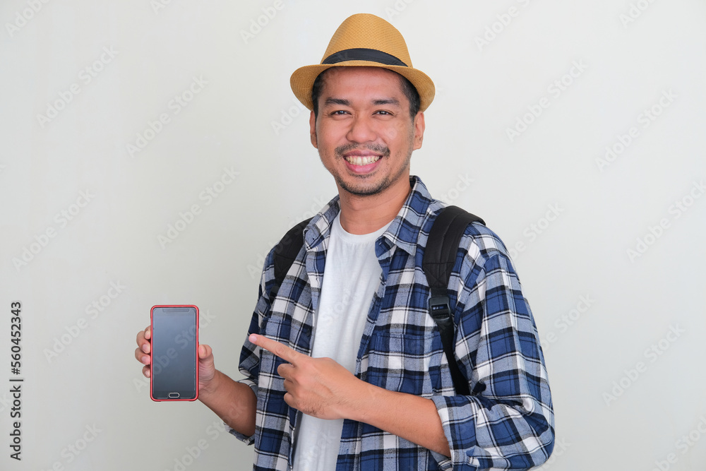 Asian backpacker smiling at the camera while pointing to blank phone screen that he hold Asian backpacker smiling at the camera while pointing to blank phone screen that he hold