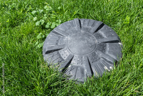 Sewer hatch on green lawn. Round black plastic cover to close access to sewer pipes. Hatch of garden communications. photo