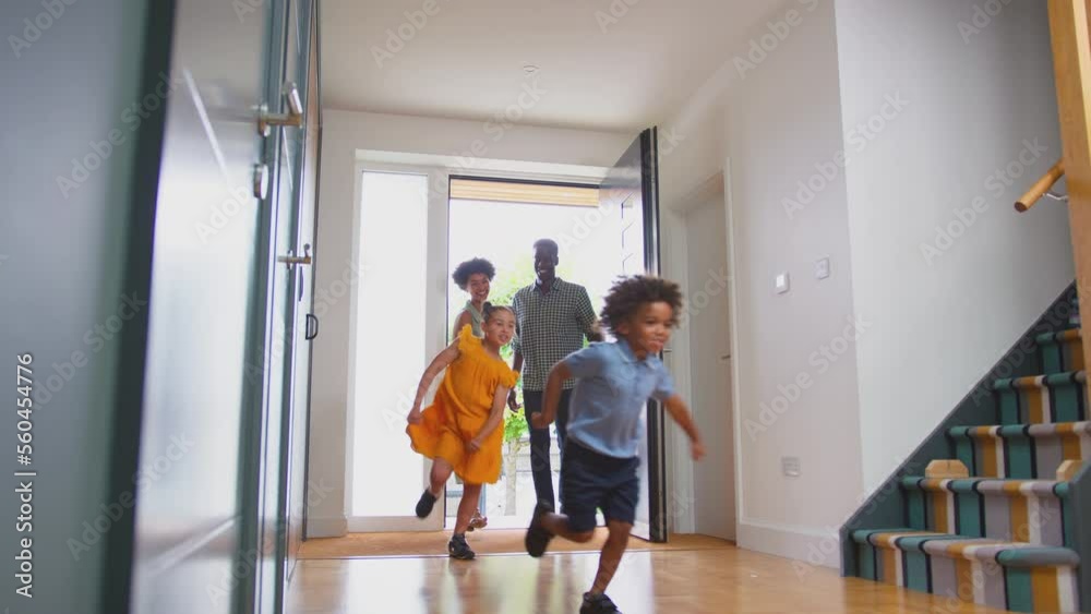 Excited children running through front door into hallway of house with parents behind as family return from trip out - shot in slow motion