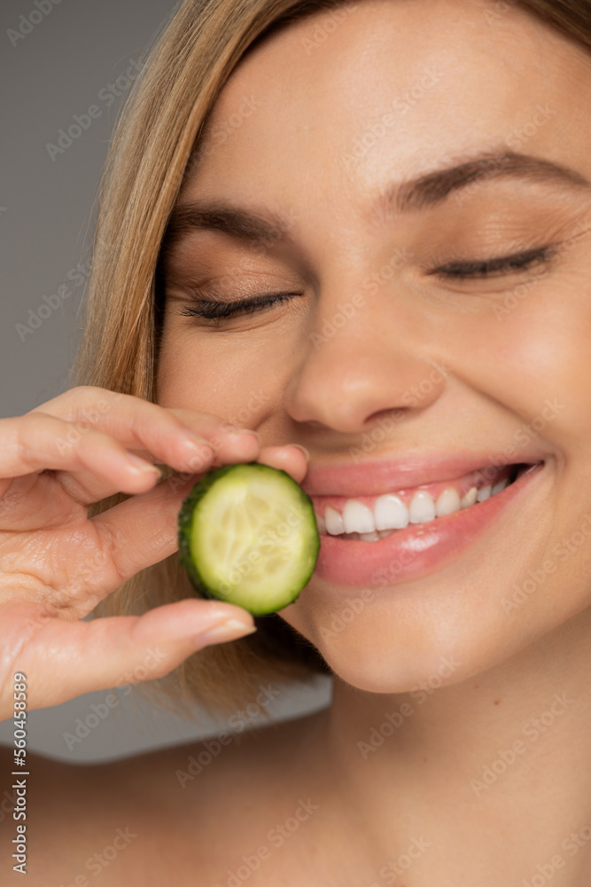 close up of cheerful woman with closed eyes holding sliced cucumber isolated on grey. close up of cheerful woman with closed eyes holding sliced cucumber isolated on grey.