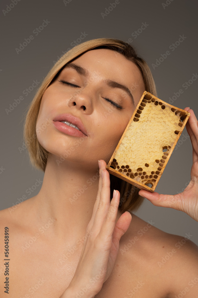 blonde young woman with closed eyes holding wooden frame with sweet honey isolated on grey. blonde young woman with closed eyes holding wooden frame with sweet honey isolated on grey.