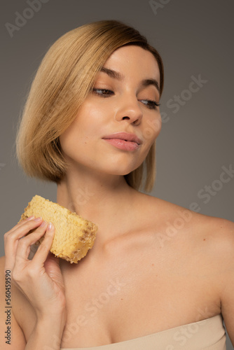 young woman holding piece of organic honeycomb isolated on grey.