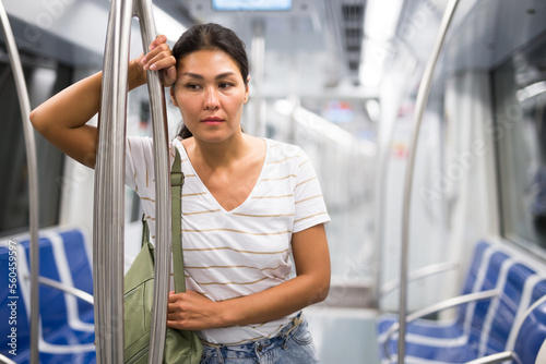 Overweary asian woman standing inside subway car and holding handrail. photo