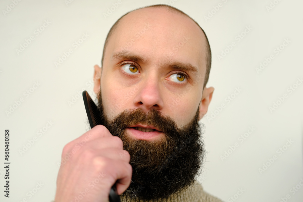 Fototapeta premium close-up of male face, young bearded and mustachioed man, guy with 25 - 30 years combs his thick beard, concept of mustache and beard stubble care products, hairline hygiene on lower part of face