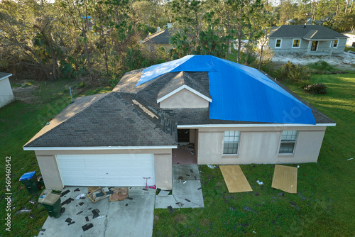 Aerial view of damaged in hurricane Ian house roof covered with blue protective tarp against rain water leaking until replacement of asphalt shingles