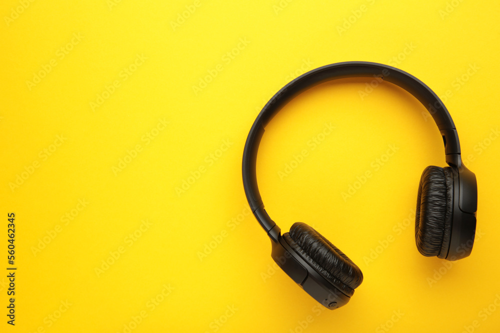 Black, modern wireless headphones on a yellow background. Black, modern wireless headphones on a yellow background.