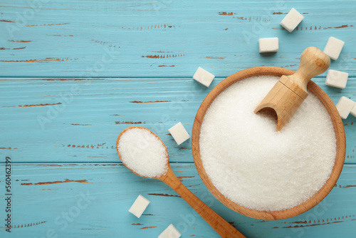 Bowl and scoop with white sand and lump sugar on blue wooden background