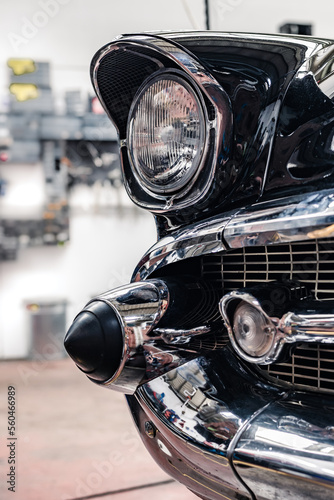 View of the headlight, grill and chrome bumper of a 1950ies classic car at a garage