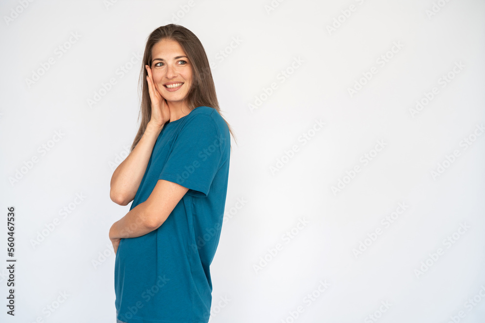 Portrait of surprised woman holding her face with hand. Female Caucasian model with brown hair and grey eyes in turquoise T-shirt and casual jeans standing aside looking amazed. Advertising concept Portrait of surprised woman holding her face with hand. Female Caucasian model with brown hair and grey eyes in turquoise T-shirt and casual jeans standing aside looking amazed. Advertising concept