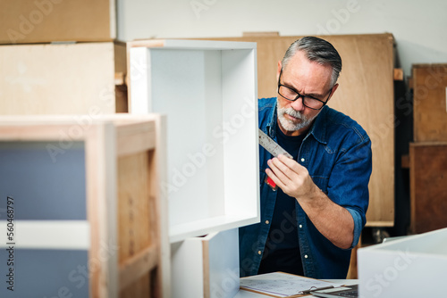 Senior caucasian man specialist worker measuring white shelf furniture in wood workshop, Small business in wood furniture industry.