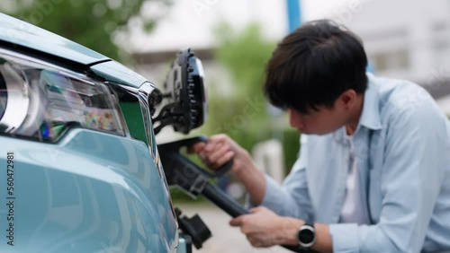 Asia man holding AC type 2 power cable plug connect to EV car at charging station. Car driven by electric motor engine for clean environment. Rechargeable vehicle concept. Ecology green technology