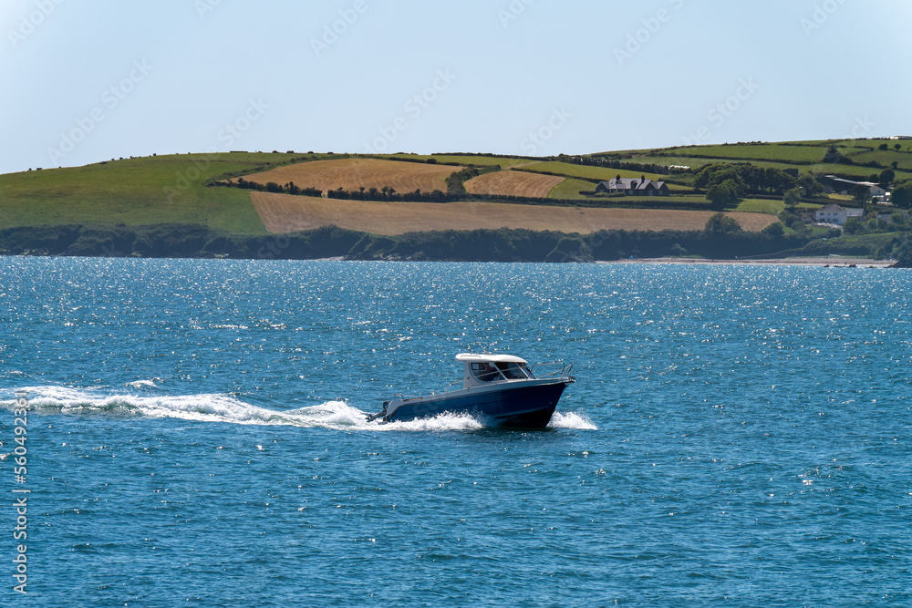 Fototapeta premium A small motor boat is sailing on the blue sea near the picturesque shores of Ireland. Seaside landscape on a sunny spring day.