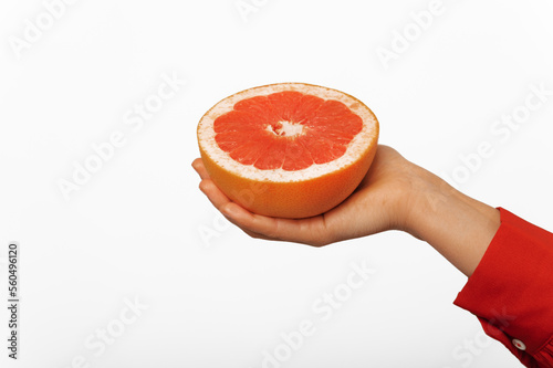 Close up shot of a female hand wearing red shirt is holds half of a grapefruit.