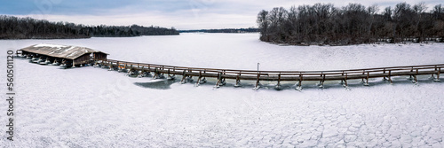 An icy dock with an old walking bridge sits on top of an snowy lake.