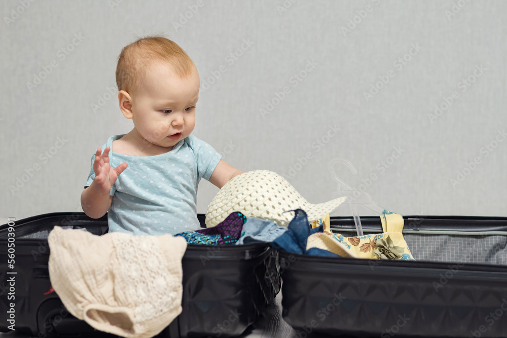 Excited baby girl sits in suitcase with clothes and gets ready for ...